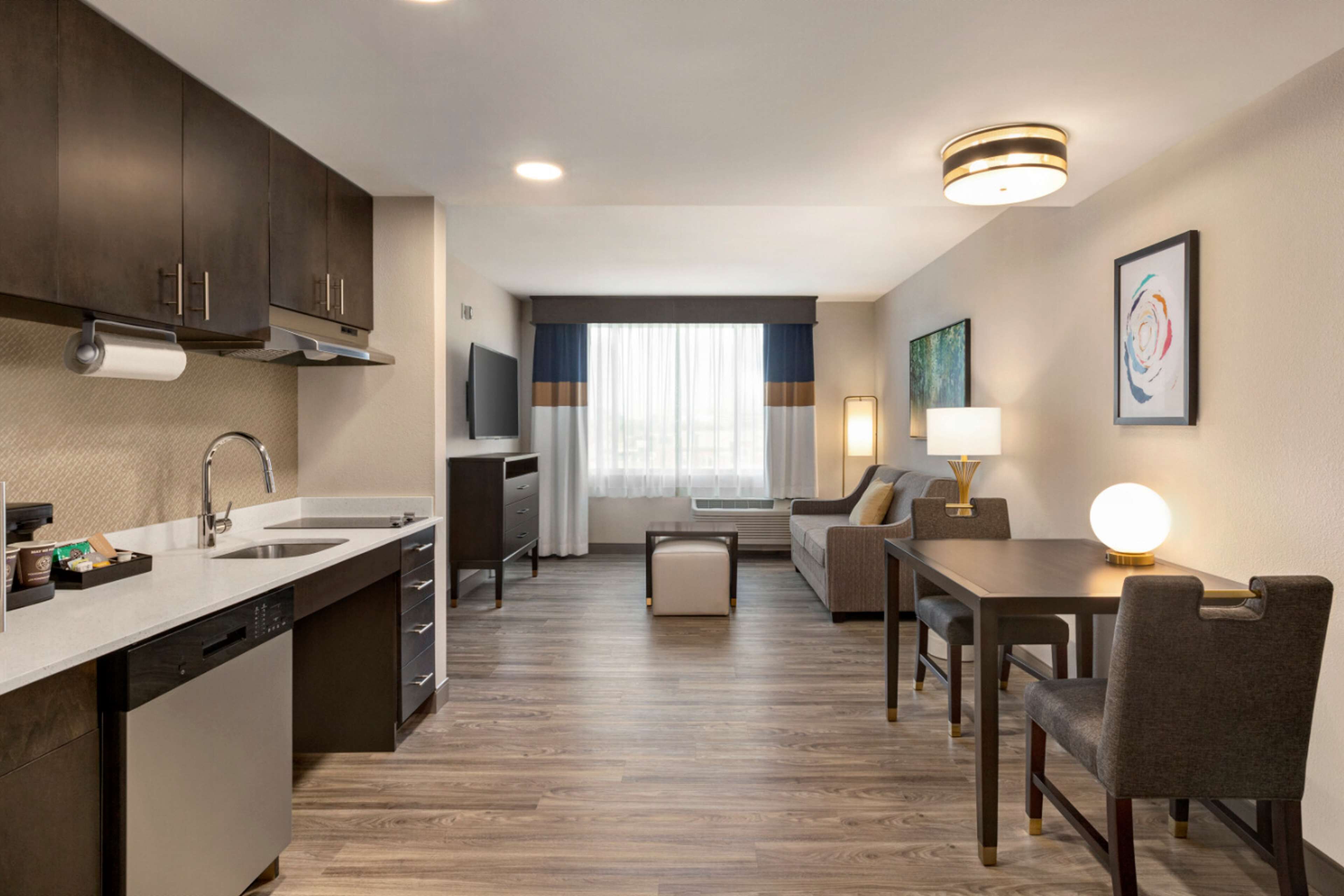 Una habitación de hotel moderna con cocina, una mesa de comedor con sillas, un sofá y un televisor.