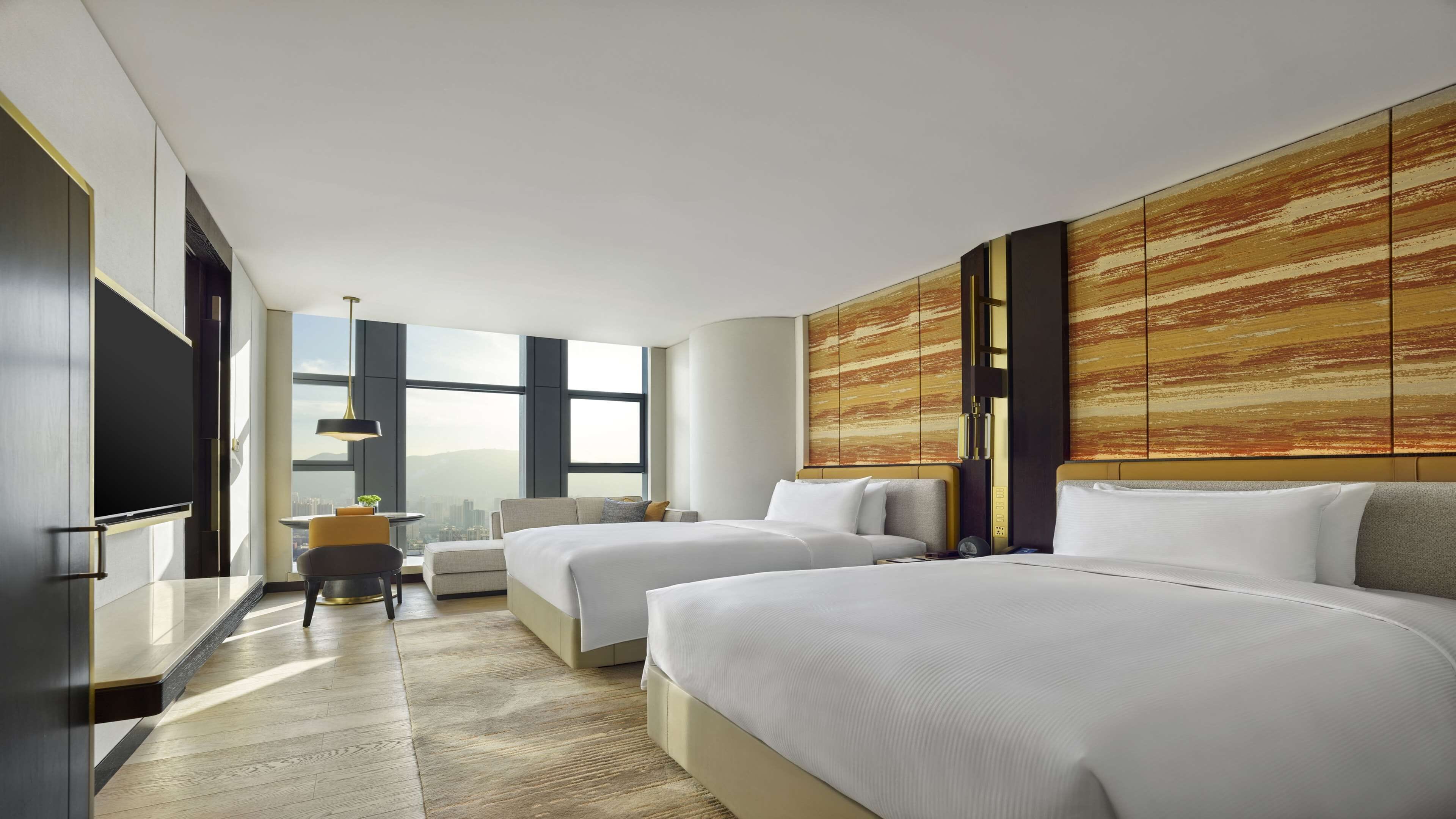 Habitación de hotel moderna con dos camas, un escritorio y un amplio ventanal con vistas a la ciudad.