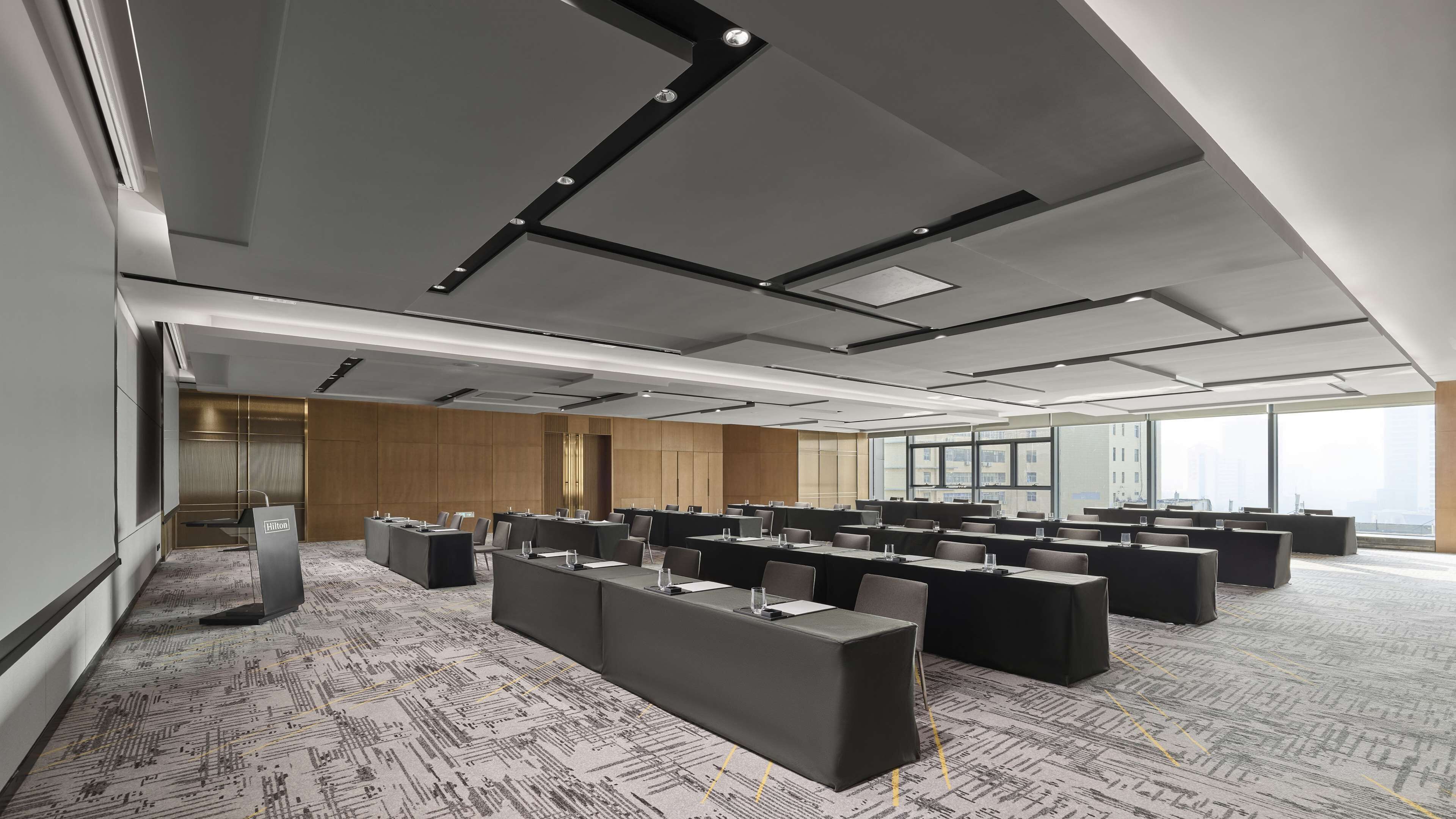 Une salle de conférence moderne, dotée de plusieurs tables et chaises, de grandes fenêtres et d’un plafond haut avec des poutres apparentes.