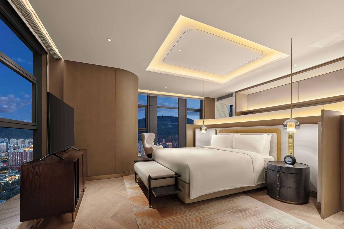Une chambre moderne avec un grand lit, un bureau et une vue sur le paysage urbain.