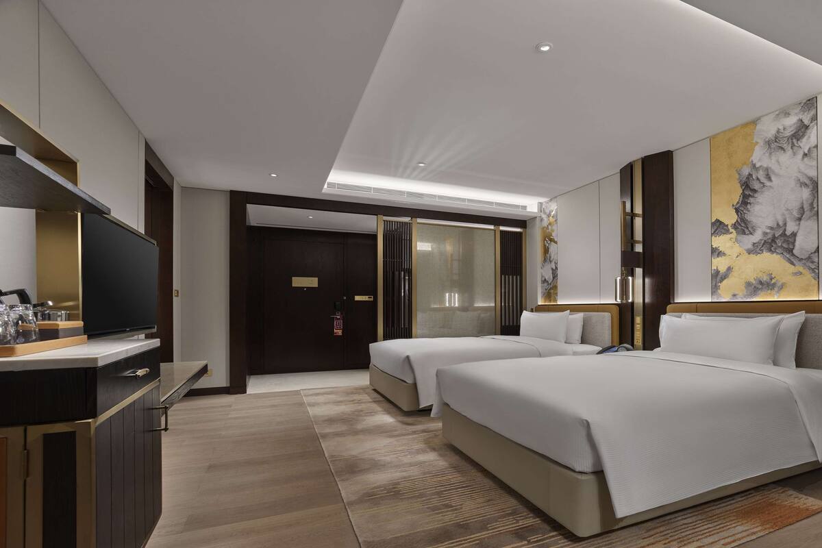 Une chambre d’hôtel moderne, dotée de deux lits, d’un téléviseur à écran plat, d’un bureau et d’un grand tableau abstrait accroché au mur.