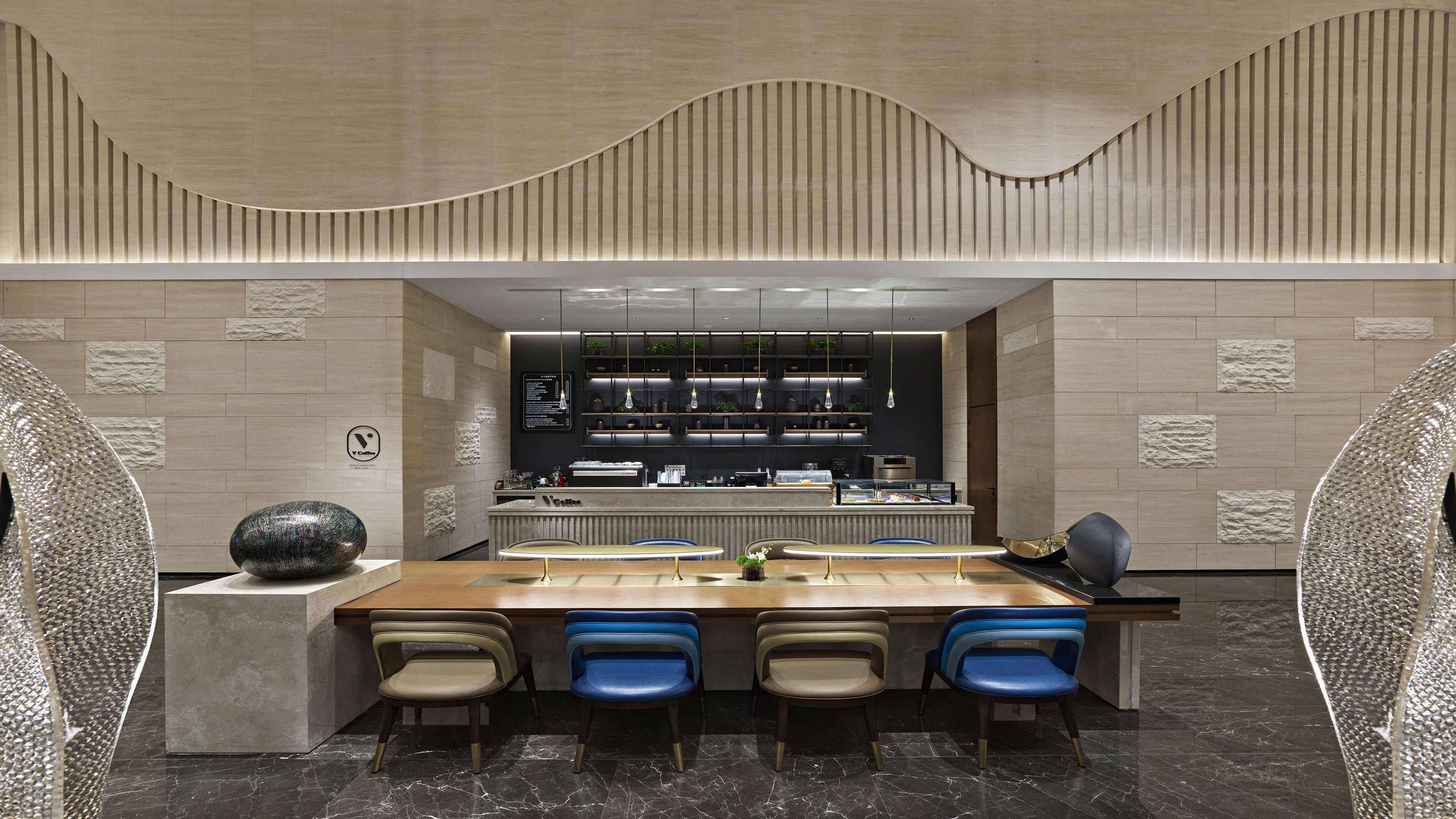 A modern restaurant with a long counter, blue chairs, and a central bar area.