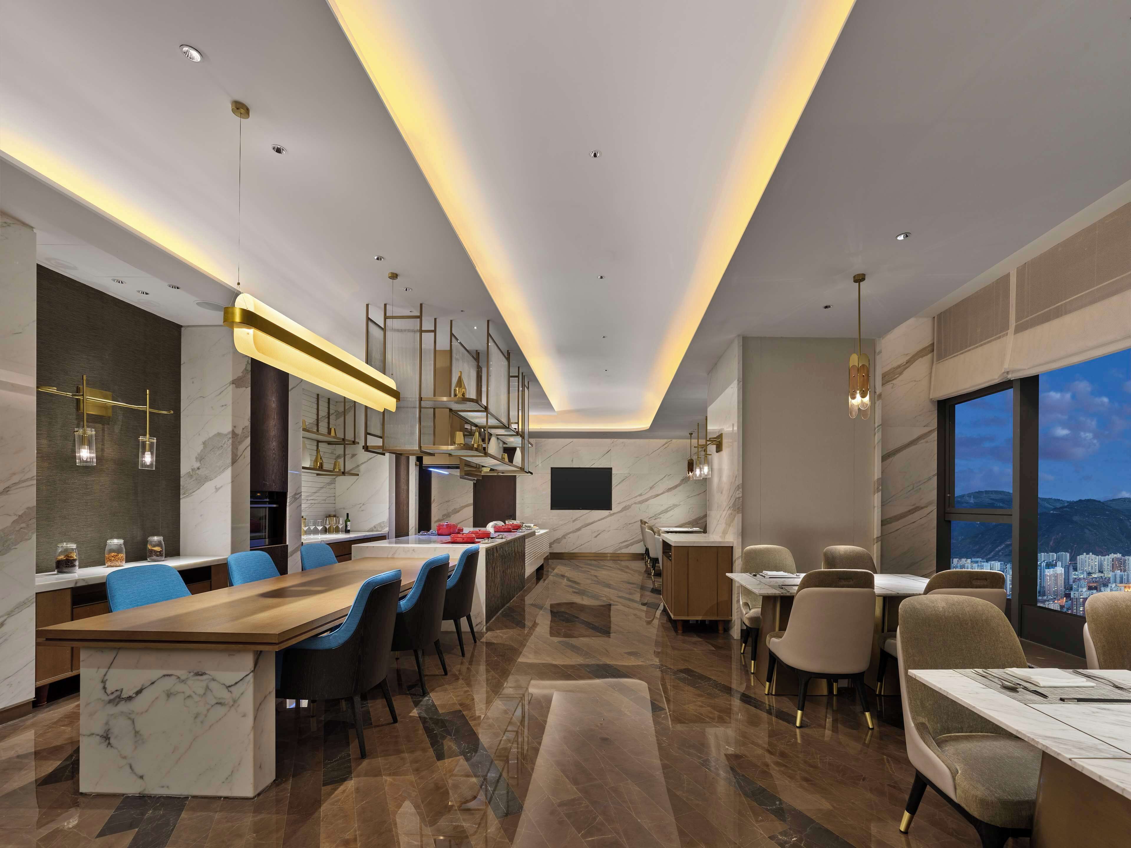Zona pranzo moderna con bancone in marmo, sedie blu e beige e lampade a sospensione.