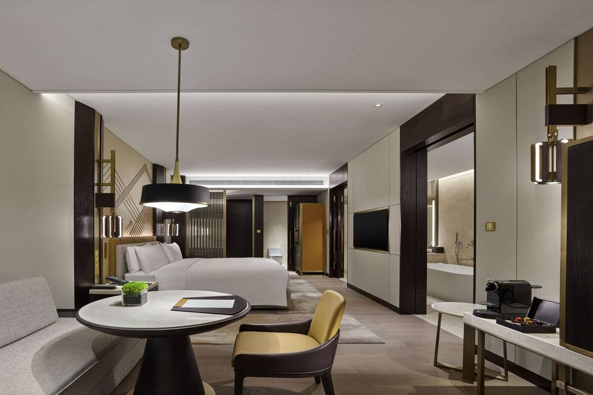 Une chambre d’hôtel moderne équipée d’un canapé, d’une table ronde agrémentée d’une plante, d’une chaise, d’un lit, d’une télévision et d’un bureau avec une machine à café.