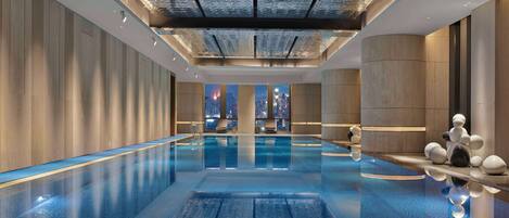 Una piscina interior moderna con vista a la ciudad, un área de descanso y un diseño de techo singular.