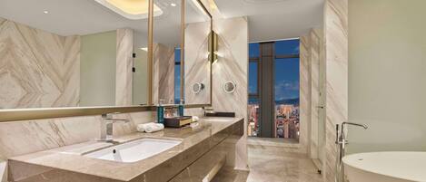 A modern bathroom with a large vanity, a bathtub, and a city view.