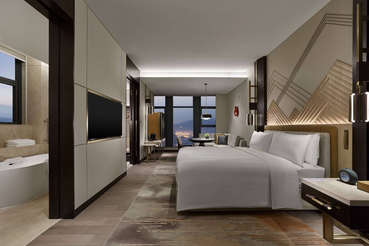 Une chambre d’hôtel moderne dotée d’un grand lit, d’une télévision, d’un bureau et offrant une vue sur la ville.