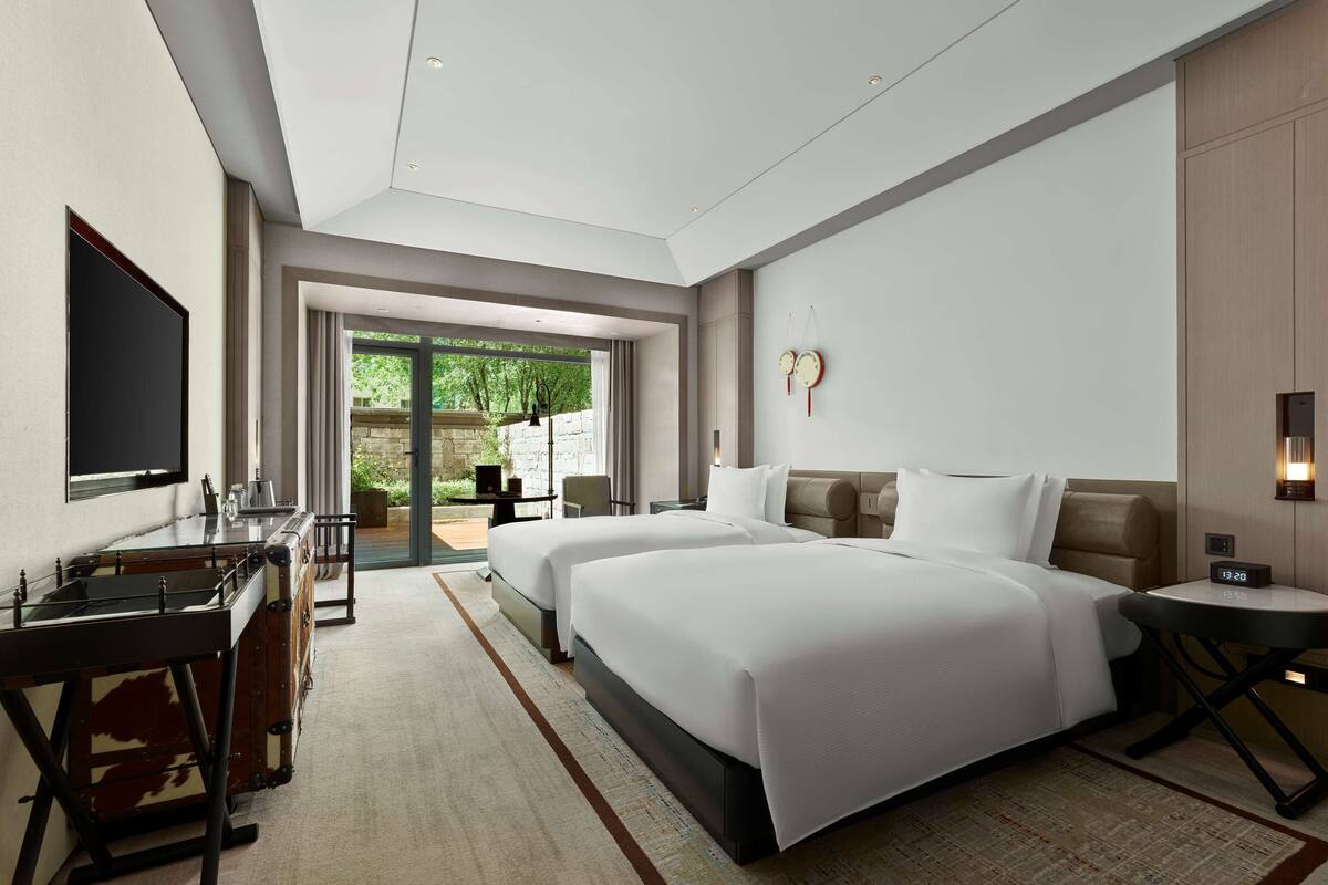 Quarto de hotel moderno com duas camas, uma escrivaninha, TV de tela plana e vista para o exterior.