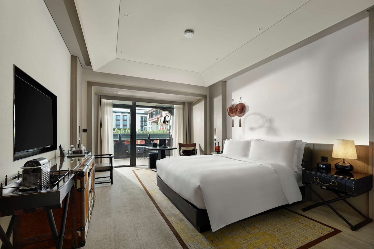 Quarto de hotel com uma cama grande, uma escrivaninha com televisão de tela plana, uma cadeira, uma mesinha e vista para o exterior.