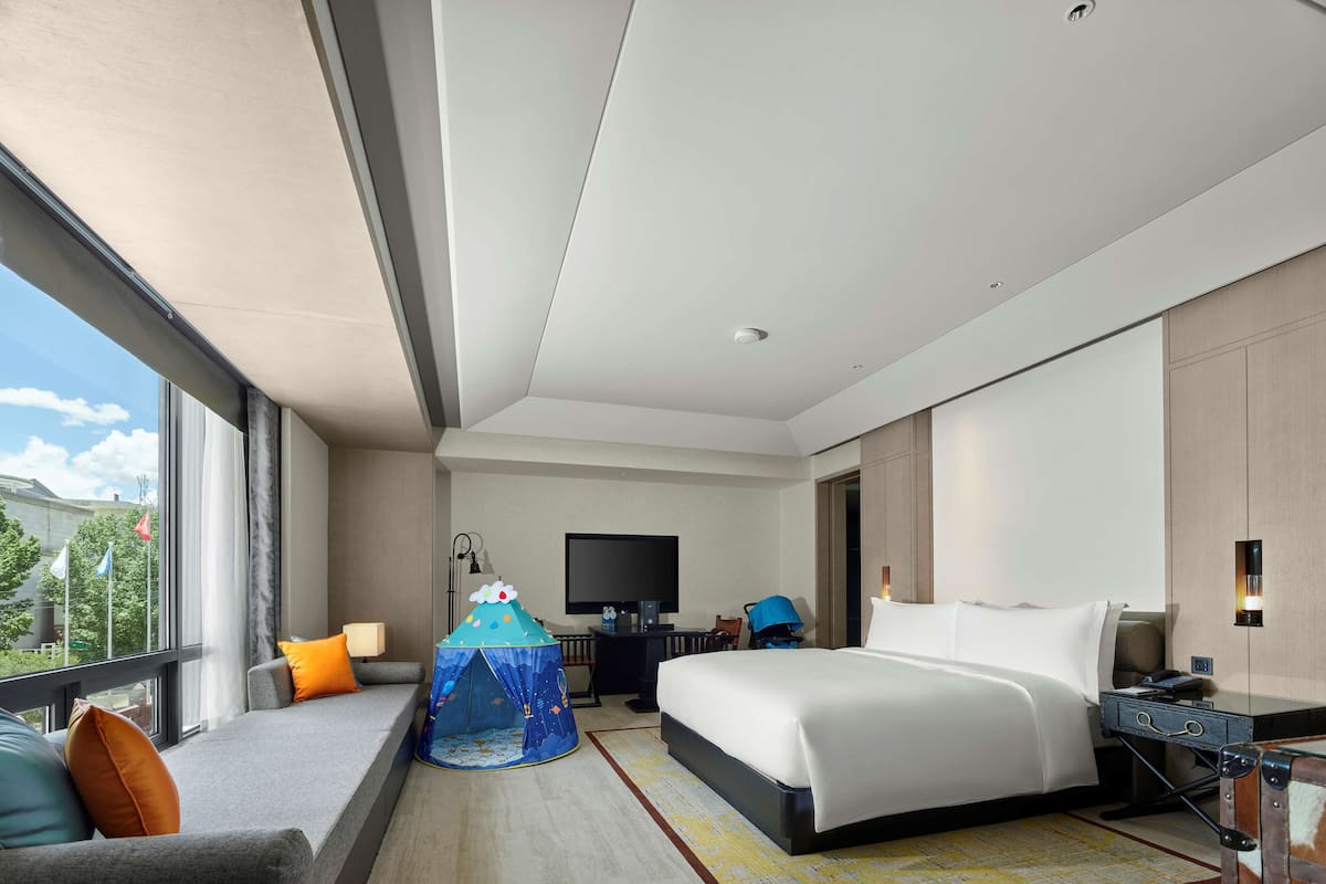 Quarto de hotel moderno com uma cama grande, uma escrivaninha, uma televisão e vista para a cidade.