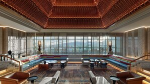 A spacious lobby with a large seating area, a patterned carpet, and a view of mountains through large windows. - Hilton Shigatse (Shigatse)