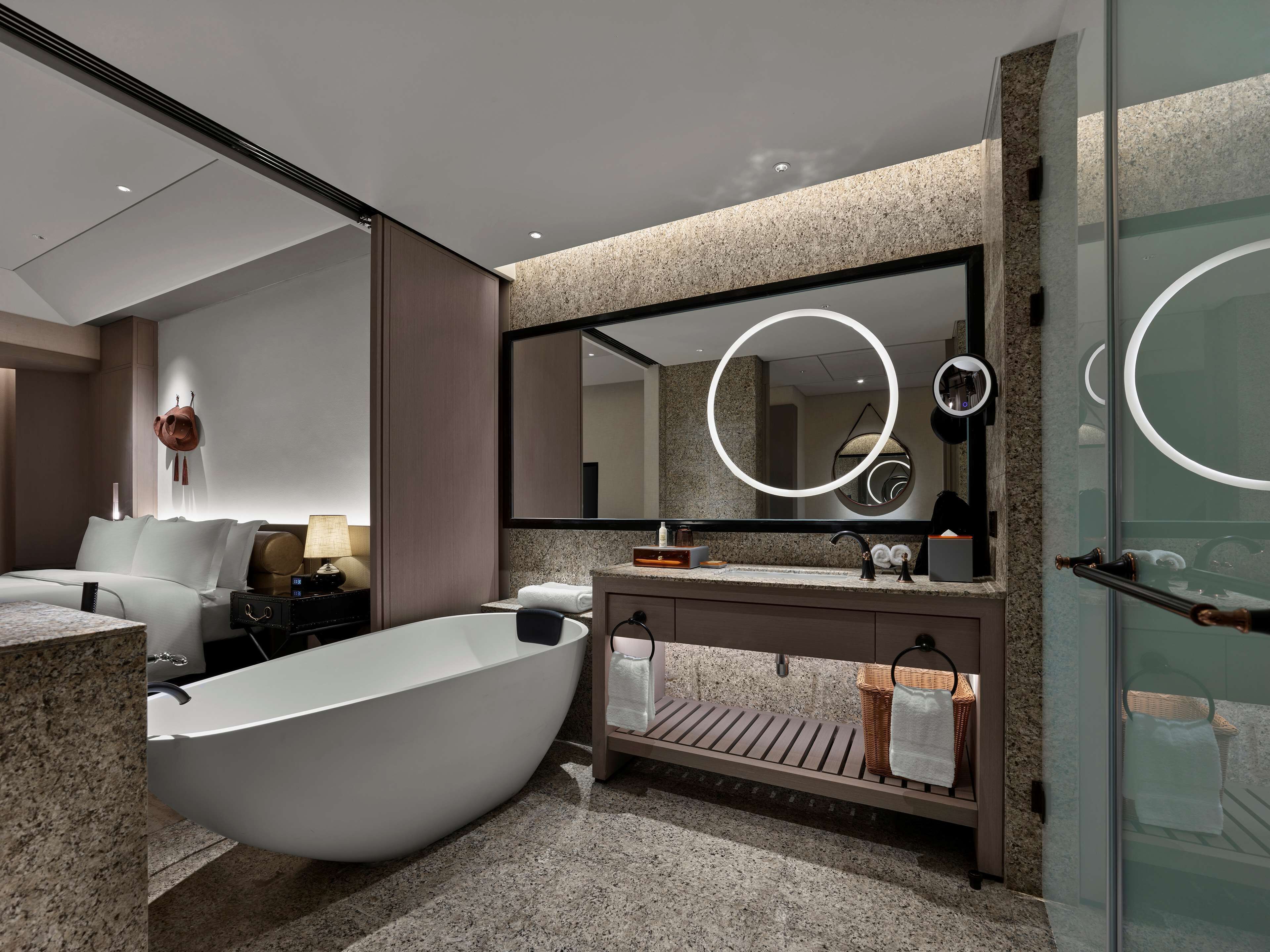 Un baño moderno con una bañera independiente, un espejo grande con luz circular y un tocador con perchero.