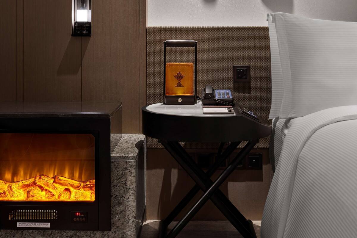 Quarto moderno com parede revestida em madeira, lareira, mesa de cabeceira com telefone e dois chapéus pendurados na parede.