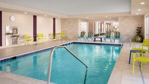 An indoor swimming pool with clear blue water, surrounded by yellow and blue chairs, and a water fountain on the left. - Home2 Suites By Hilton Tupelo, Ms (Tupelo)