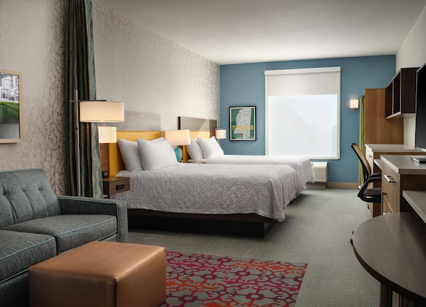 Quarto de hotel com duas camas, um sofá, uma escrivaninha e uma cadeira.