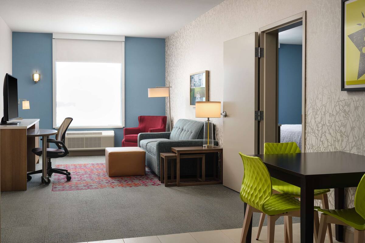 Hotellihuoneessa on työpöytä, punainen tuoli, harmaa sohva, vihreä tuoli ja sänky.