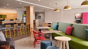 A modern lounge area with a green sofa, red chairs, and a wooden table. - Home2 Suites By Hilton Tupelo, Ms (Tupelo)