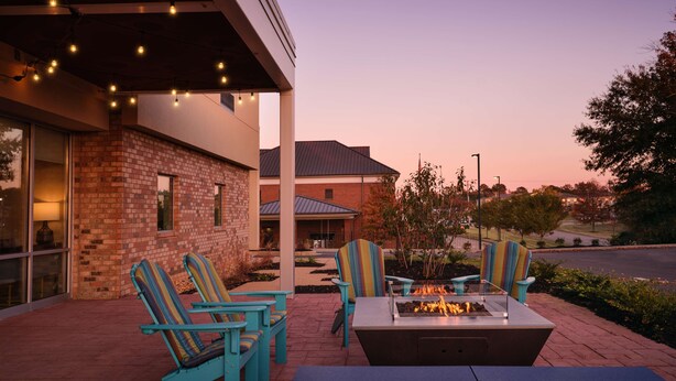 An outdoor seating area with chairs and a fire pit, a brick building, and a clear sky. - Home2 Suites By Hilton Tupelo, Ms (Tupelo)