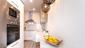 Cozinha moderna com forno embutido, exaustor de aço inoxidável e bancada de mármore. Há uma cesta de limões na bancada e um banquinho pequeno.