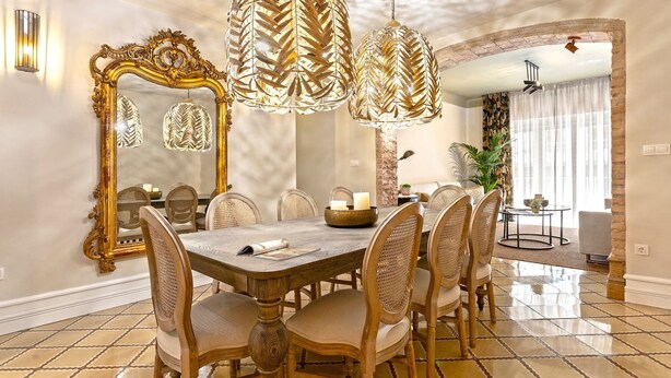 Uma área de refeições com uma grande mesa de madeira, seis cadeiras e um espelho decorativo.