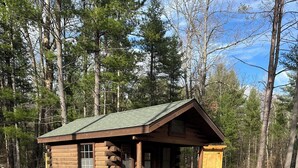 A rustic log cabin with a porch and a picnic table in a wooded area. - Log Cabin Sleeps four (Big Rapids)