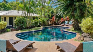 Una piscina circondata da piante tropicali e una casa con un portico coperto.