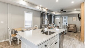 A modern kitchen with a central island, white cabinetry, and a dining area with a wooden table and chairs.