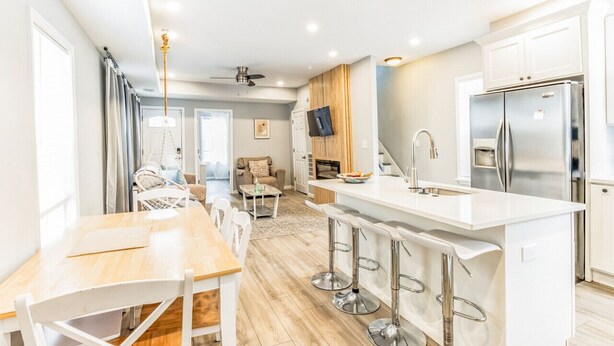 A modern kitchen with white cabinetry, a stainless steel refrigerator, and a bar area with stools.