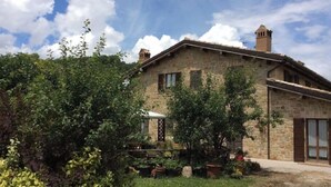 A stone building with a sloped roof and two chimneys, surrounded by lush greenery and potted plants. - I Girasoli - Red apartment (San Marcello, Camerino)