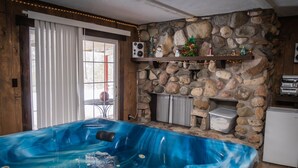 A room with a stone fireplace, a hot tub, and a small kitchen area.
