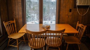A wooden dining table with four chairs, a window with a view of a snowy landscape, and a wall-mounted air conditioner.