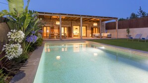 Ein modernes Haus mit Swimmingpool, Sitzgelegenheit im Freien und einer Steinfassade.