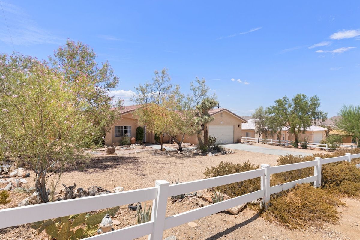 A residential area with houses, a white fence, and desert vegetation.