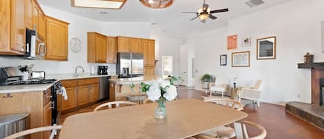 A modern kitchen with wooden cabinets, a dining table with chairs, a ceiling fan, and a vase with flowers.