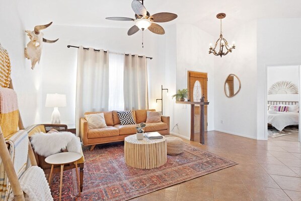 A living room with a sofa, a round coffee table, a chandelier, a ceiling fan, and a large rug.