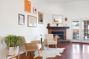 Een woonkamer met een open haard, ingelijste foto's, een potplant en een wit tapijt.