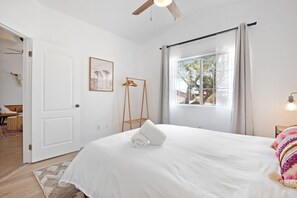 A bedroom with a bed, a window with curtains, a ceiling fan, and a bedside table with a lamp.