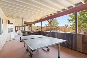 Un espace extérieur abrité comprenant une table de ping-pong, des sièges et une vue sur le jardin.
