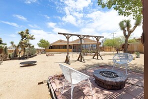 A backyard with a swing set, a fire pit, and a patio chair.