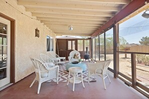 Une terrasse couverte, aménagée avec des meubles en osier, une table ronde centrale et offrant une vue sur le paysage environnant.