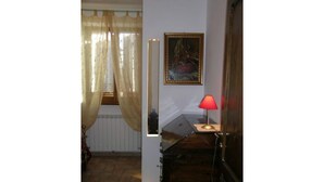 Een kamer met een piano, een rode lamp, een lijst met een foto aan de muur, en een raam met dunne gordijnen.