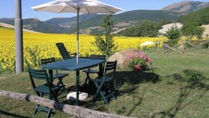 Een tafel met stoelen en een parasol in een veld vol gele bloemen, met bergen op de achtergrond.