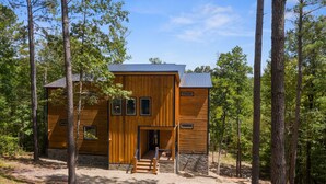 Una cabaña moderna de madera con base de piedra, rodeada de árboles altos.