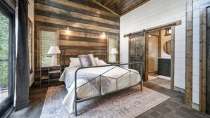 Un dormitorio con estructura de cama metálica, paredes de madera y un ventanal grande.