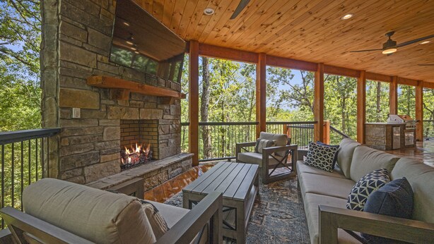 Un espacio al aire libre techado con chimenea de piedra, muebles de madera y vistas al bosque circundante.