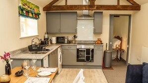 A compact kitchen with grey cabinets, a microwave, oven, and a sink. There's a dining table with chairs and a vase of flowers. - The Old Mower Shed (Grantham)