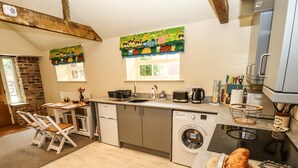 A compact kitchen with a washing machine, a toaster, and a wooden dining table with chairs. - The Old Mower Shed (Grantham)