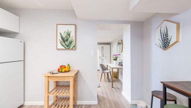 A modern kitchen with a wooden table, a fruit bowl, and a framed succulent plant.