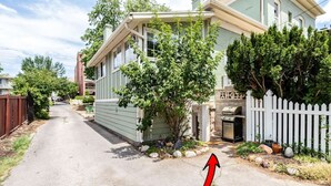 A residential street with a house featuring a front yard, a barbecue grill, and a white picket fence.