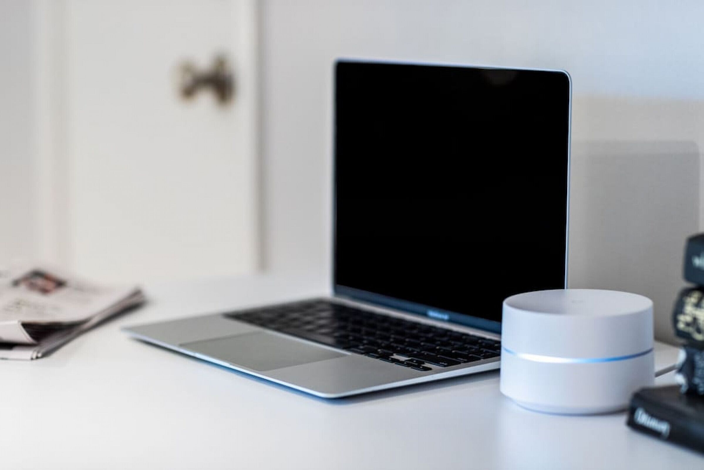A laptop on a white desk with a white cylindrical object beside it.